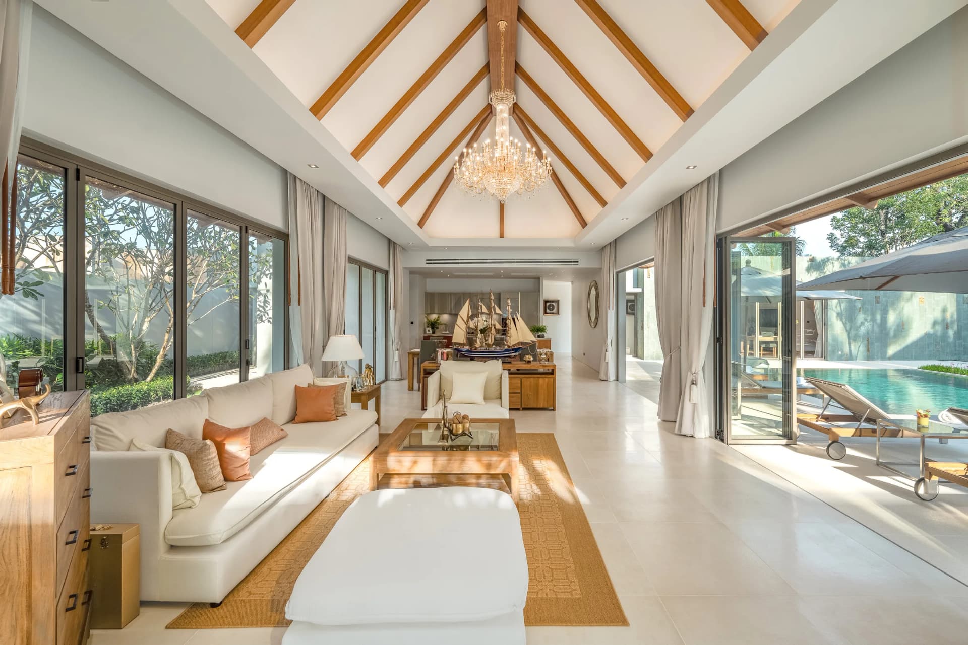 Living room under a vaulted teak ceiling, glazed to the pool — built Anchan villa, same design team and materials